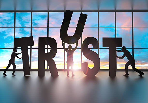 silhouettes of business partners moving letters inside an office at sunset. They are building the word trust